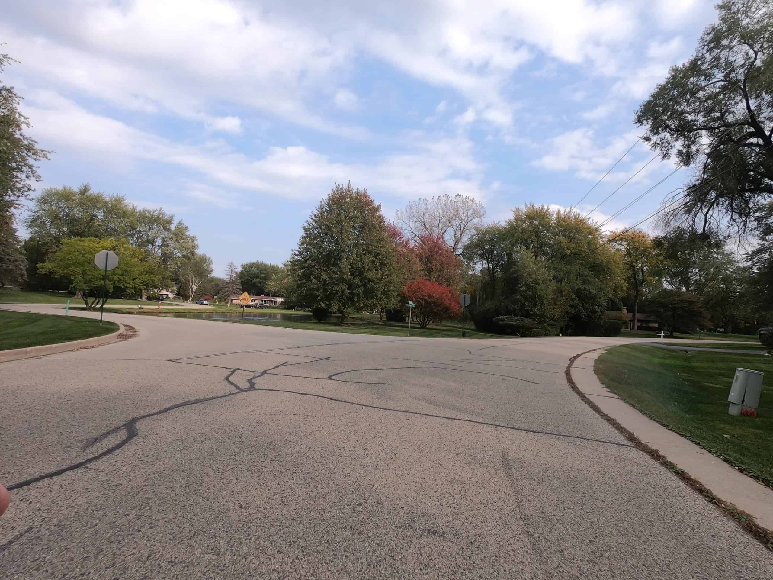 Looking down a wide street in a spacious, tree and meadow lined neighborhood.