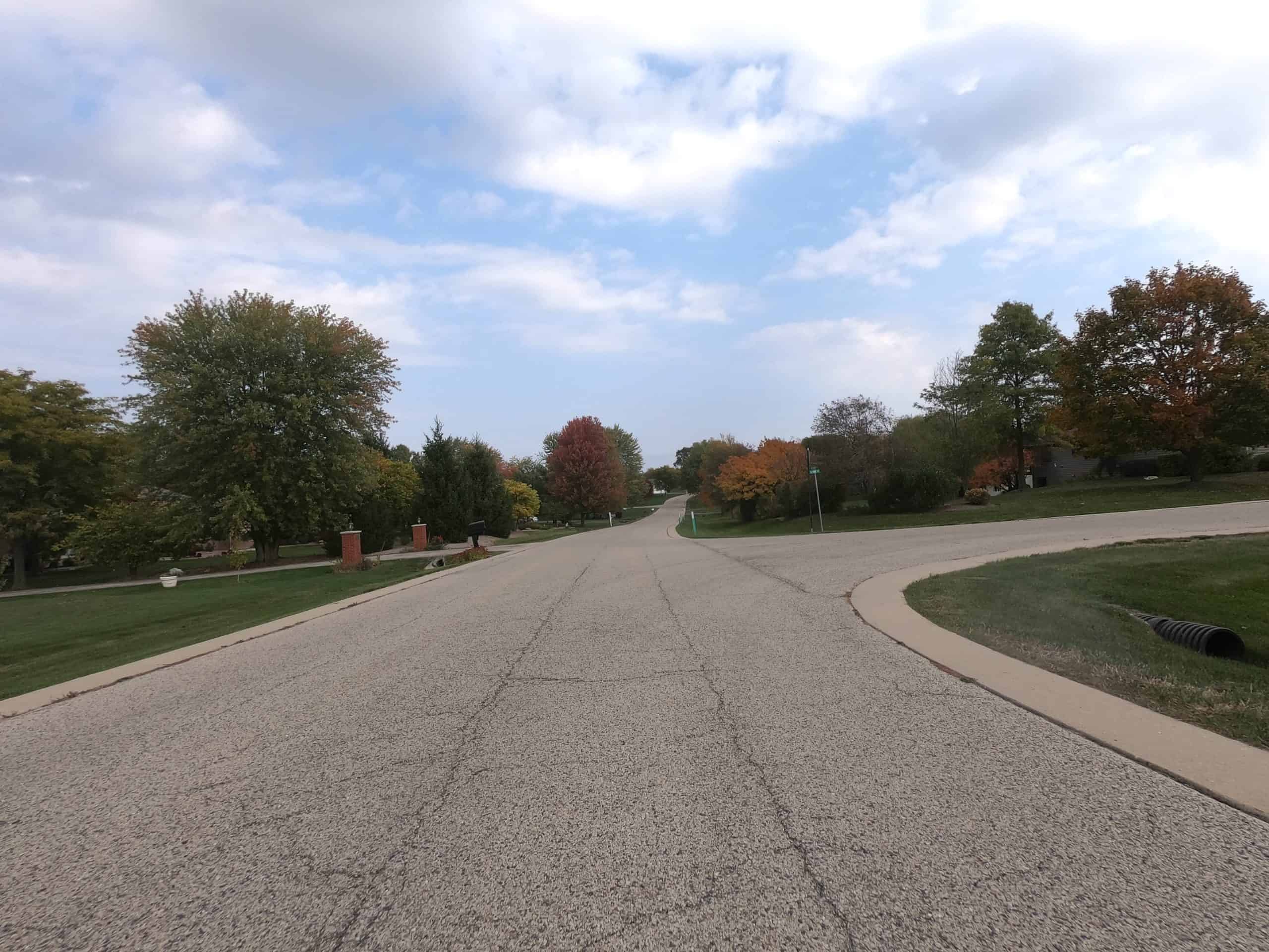 Looking down a wide street in a spacious, tree and meadow lined neighborhood.