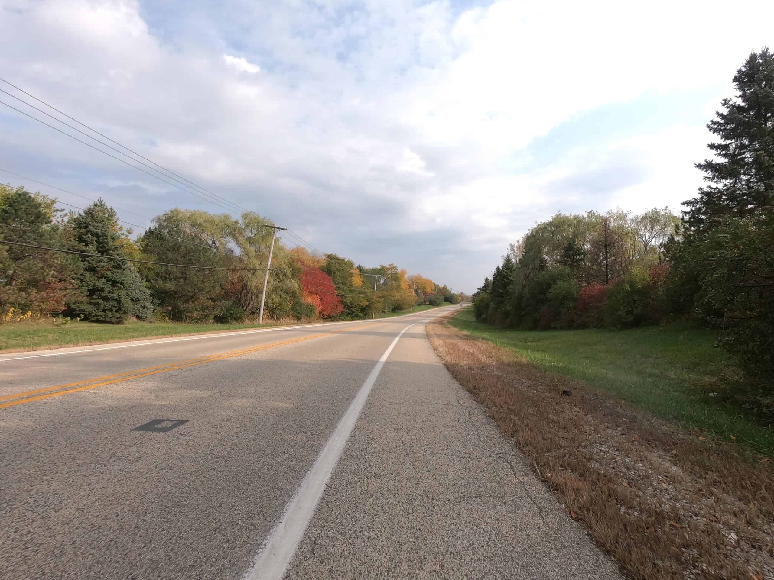 Looking down a colorful tree and meadow lined two-lane road.