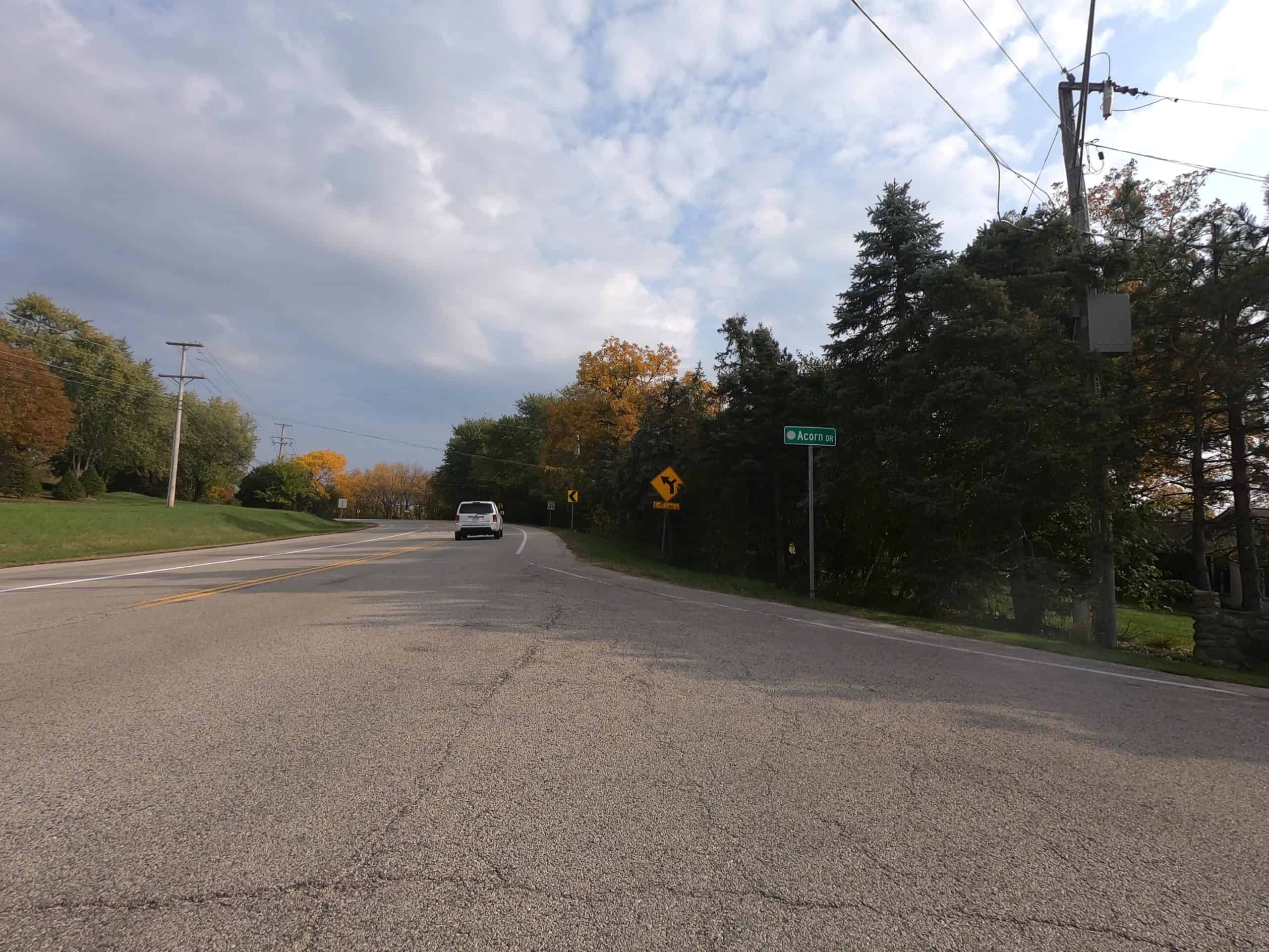 Looking down a colorful tree and meadow lined two-lane road at an intersection with a sidestreet.