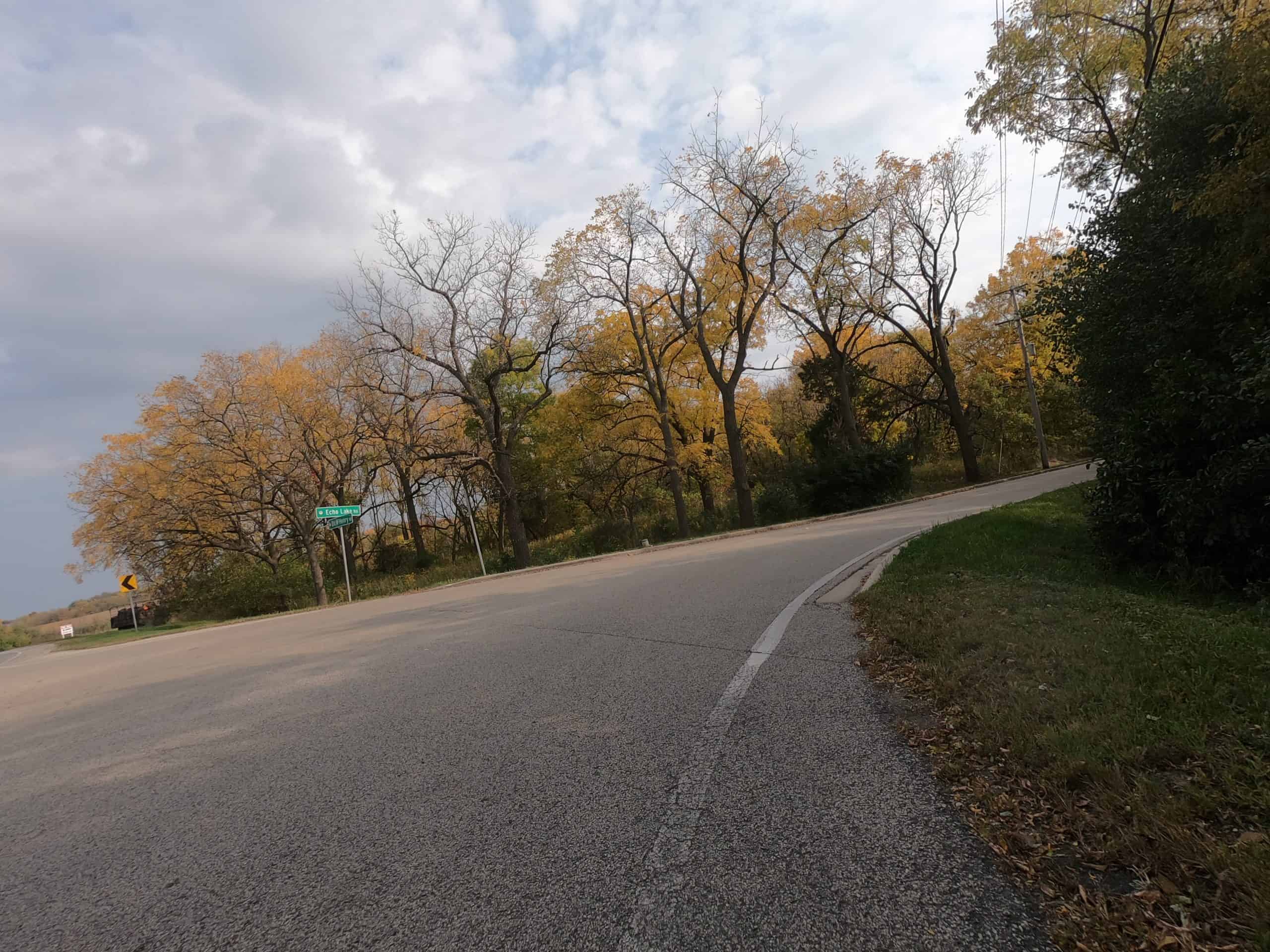 Looking down a colorful tree-lined two-lane road on a curve at an intersection.