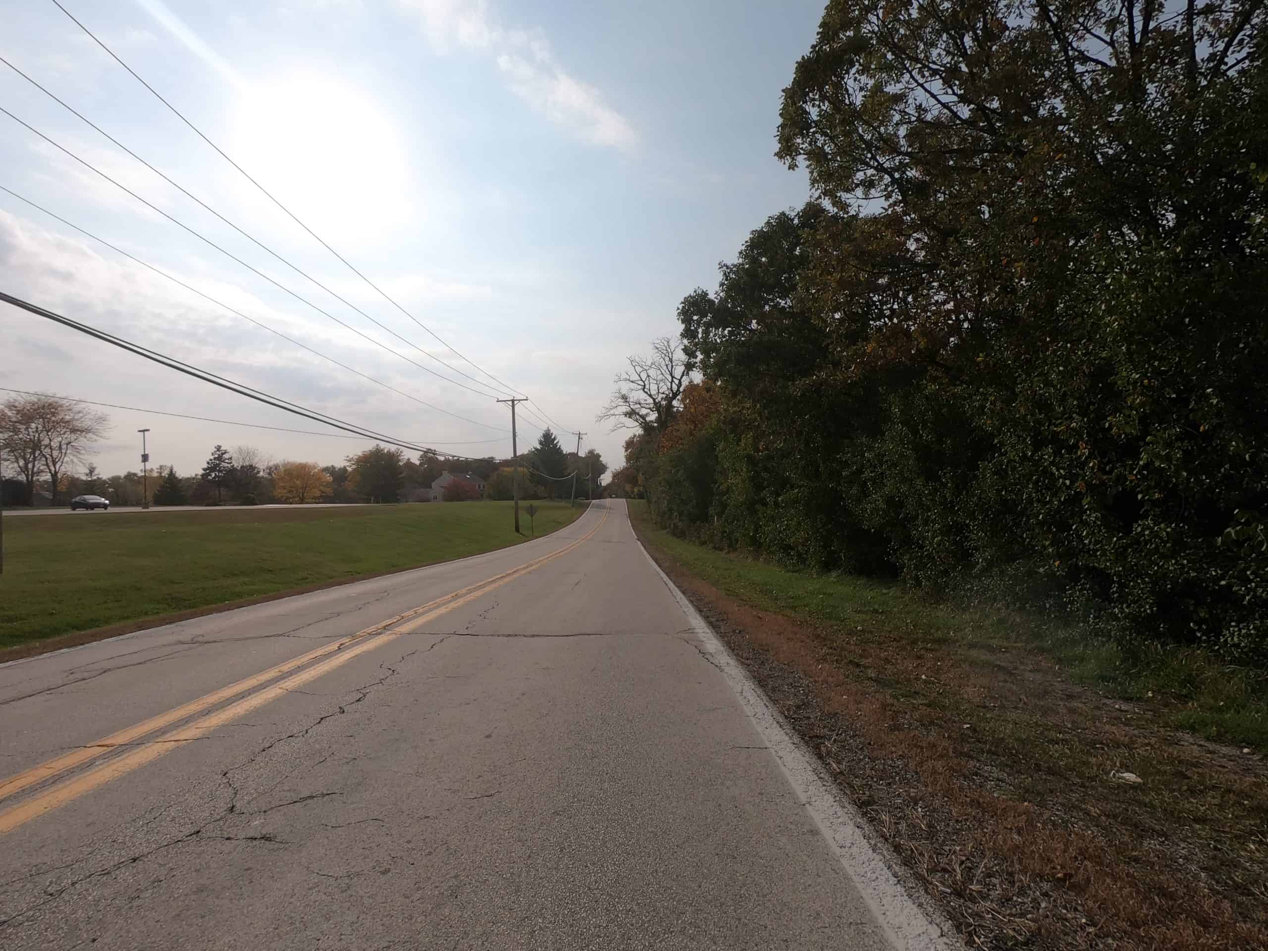 Looking down a colorful tree and meadow lined two-lane road.