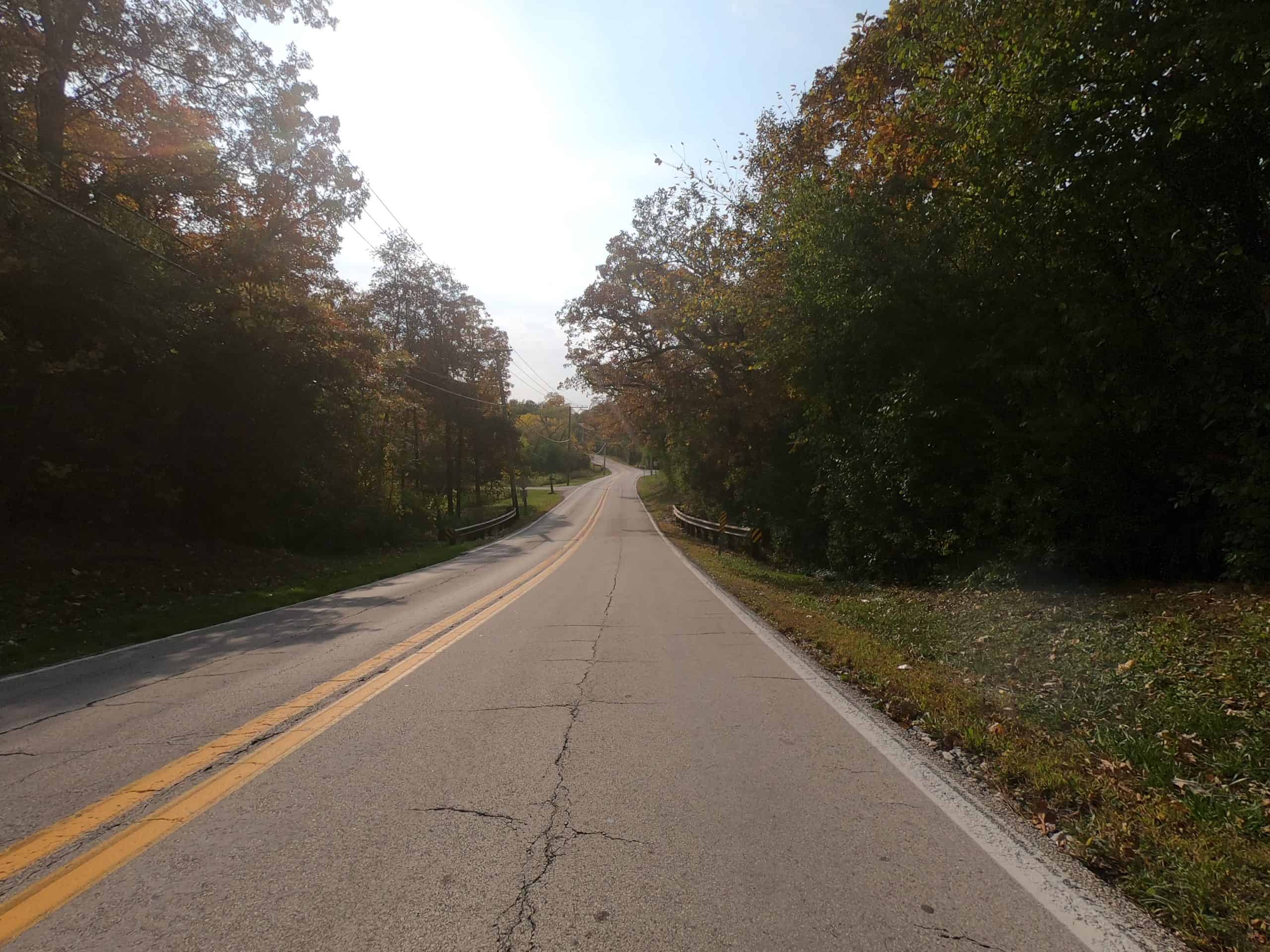 Looking down a colorful tree-lined two-lane road.