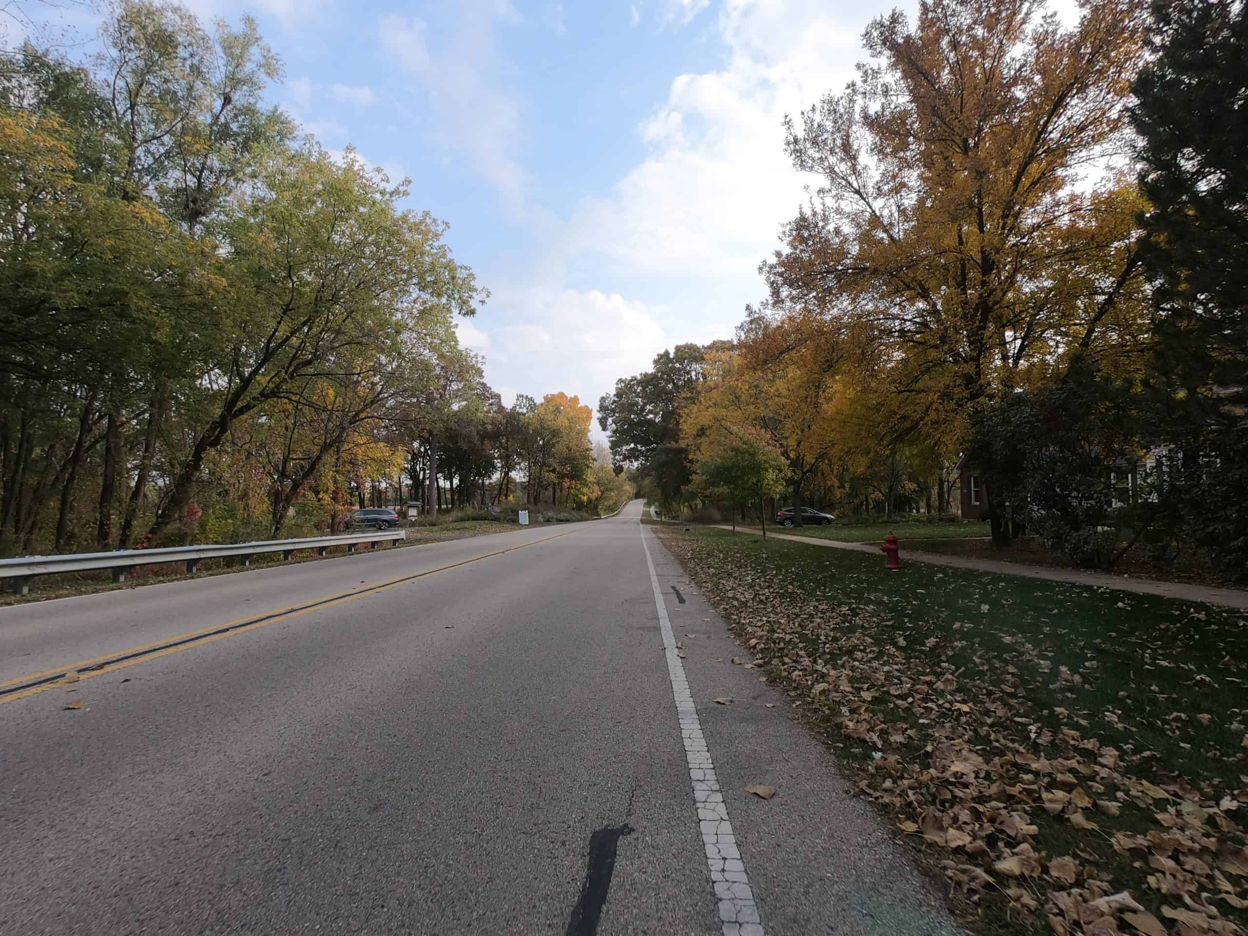 Looking down a colorful tree-lined two-lane road.