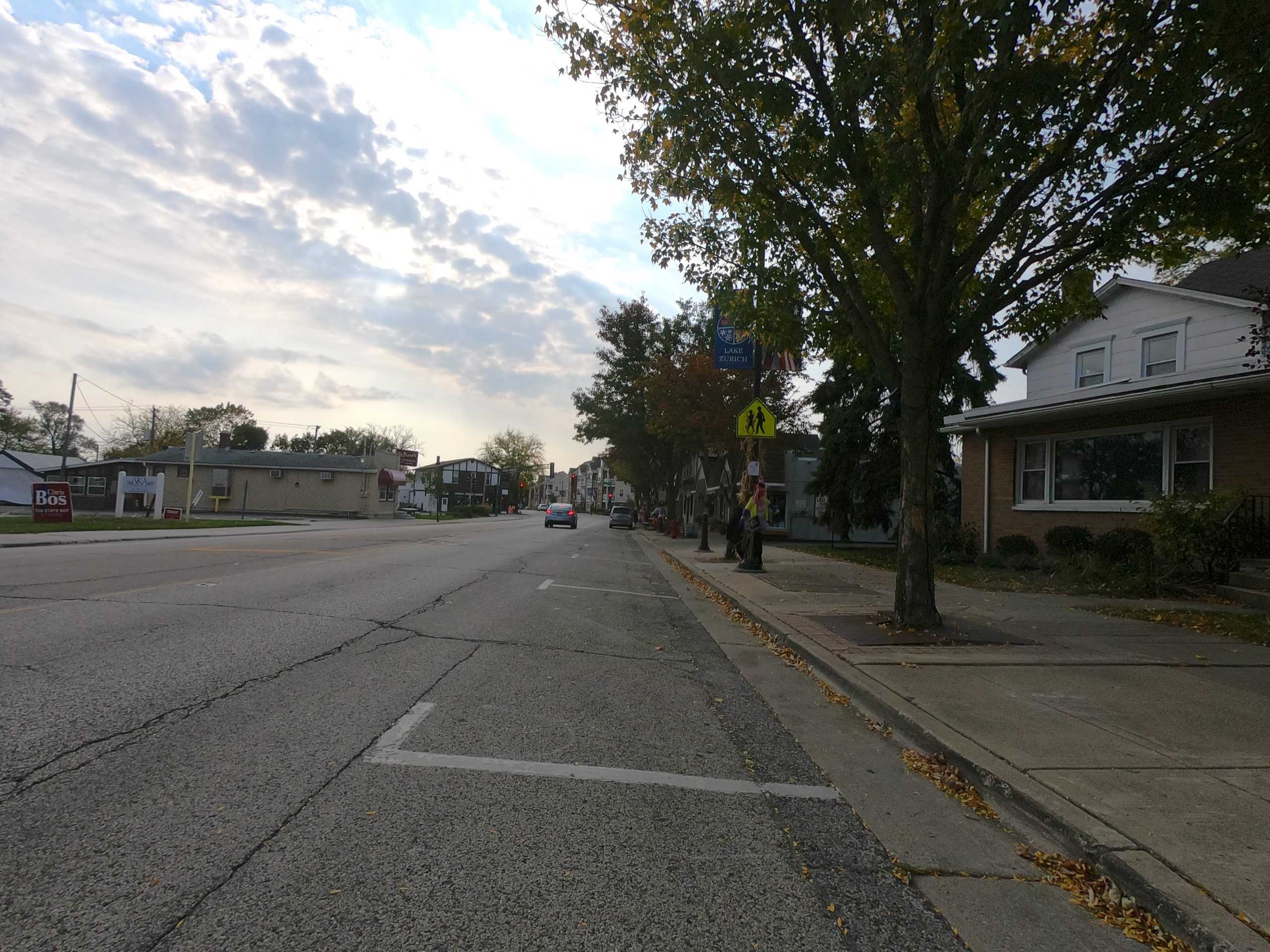 Looking down a small-town downtown street and open parking spaces, car in the distance.