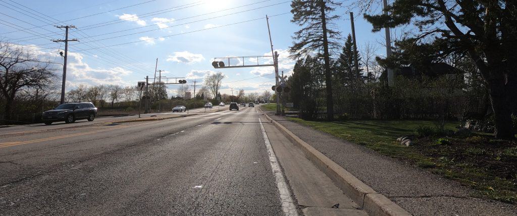 Looking down a four-lane road with some cars on a sunny day with a railroad crossing ahead.