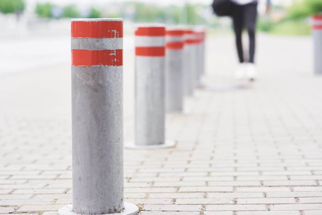 A line of bollards, two orange-red stripes atop each one, on brick pavement.
