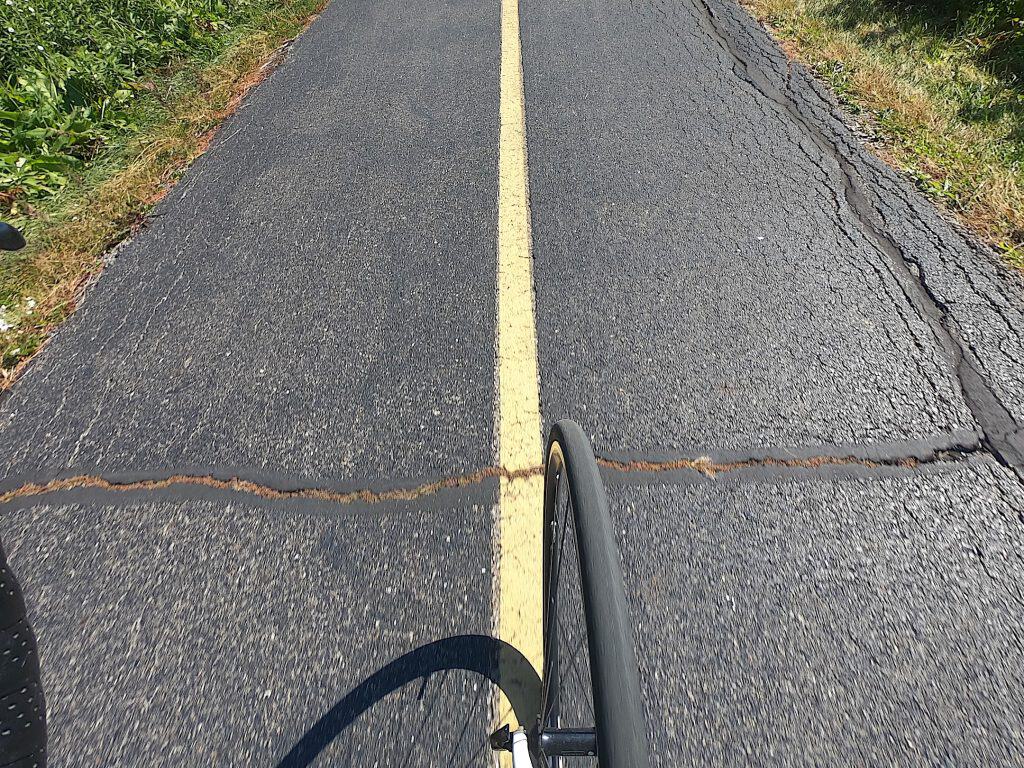 A bike wheel is seen up close over a striped bike path, crossing a big crack.