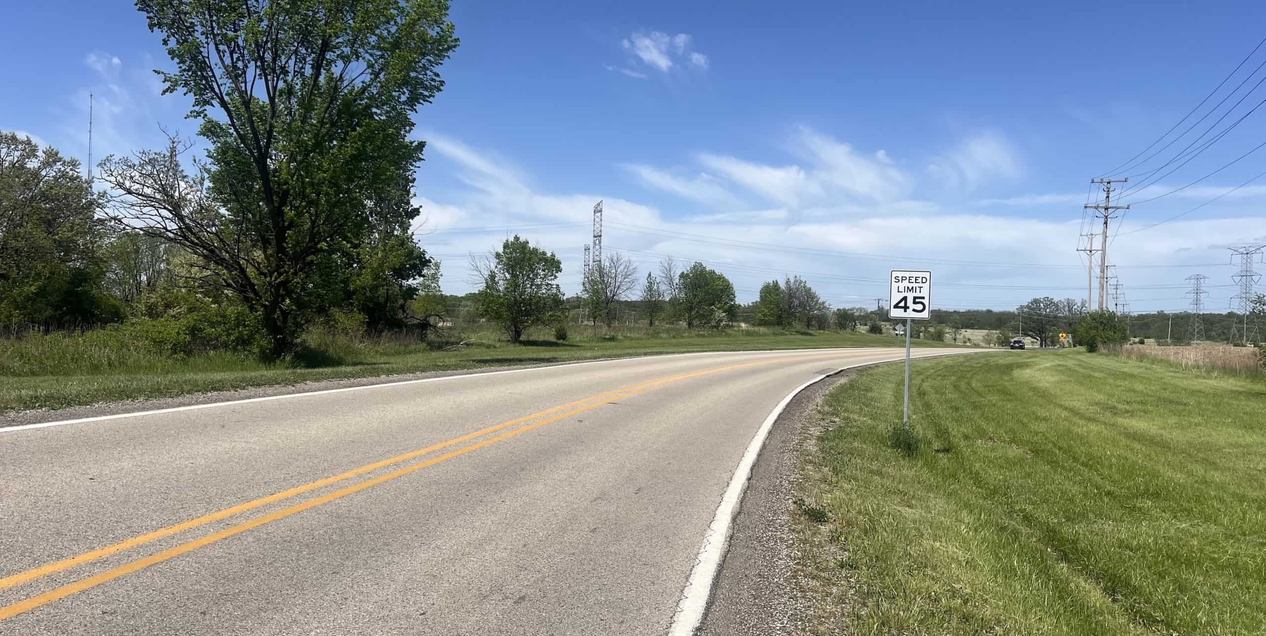 Looking down a paved road curving right in a remote area with some trees and grass in the background.