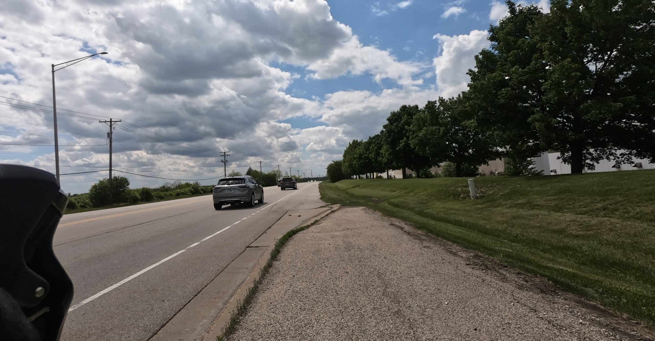 A path before us is about to end and blend into the shoulder of a wide road with lawn and short trees on the right side.