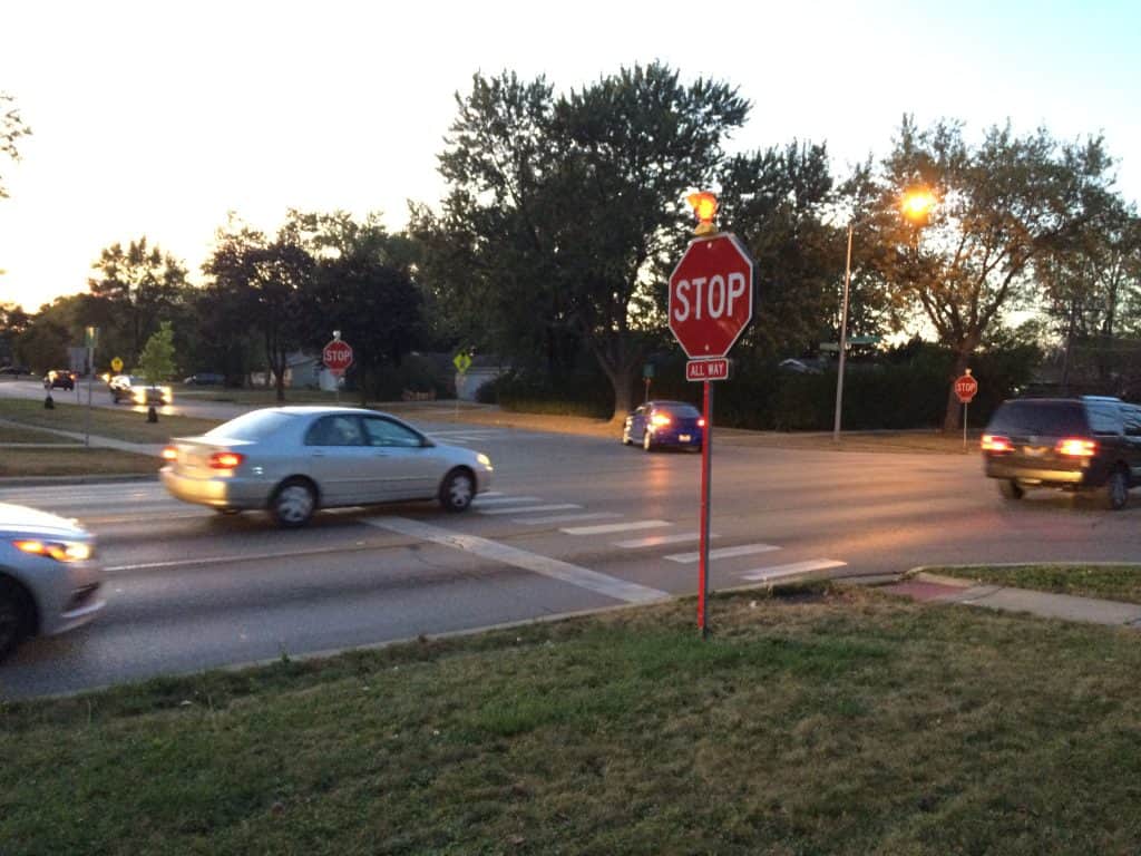 Cars dash through stop signs at an intersection in a suburban intersection during twilight.
