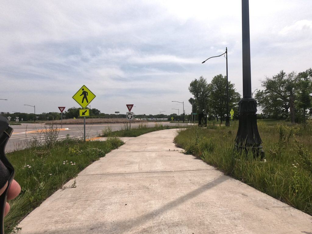 Looking at a concrete path about to enter a roundabout with crosswalks in an open area.