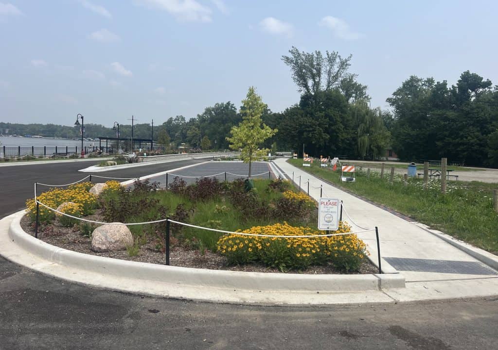 Looking at a median with flowers with a new sidewalk on the right and new paved road on the left.