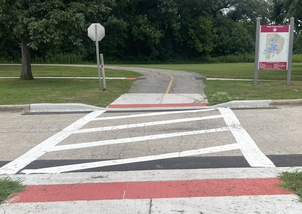 Bike path crossing in suburban Chicago with signage and greenery.