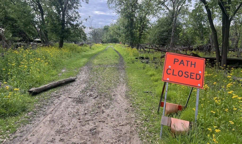Bike trail closed sign on a rustic dirt and gravel bike path surrounded by trees and wildflowers in suburban Chicago.
