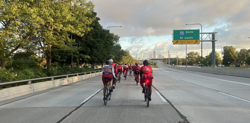 Bicyclists cycling on a Chicago lakefront highway with city skyline in the background.