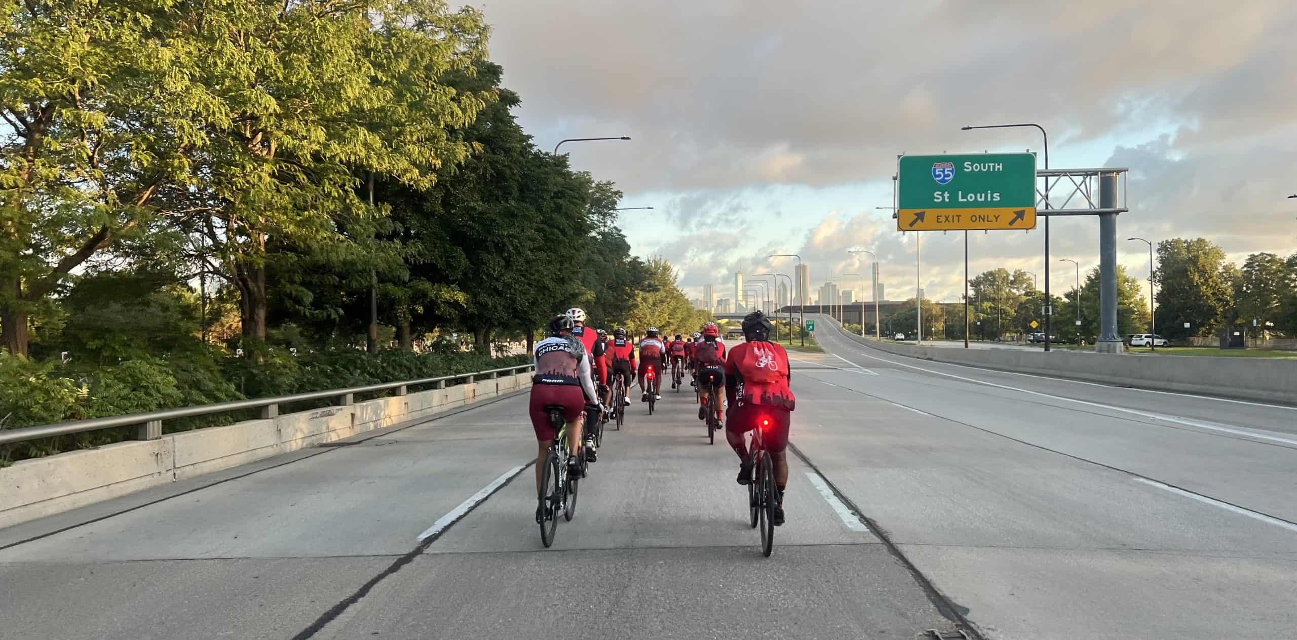 Bicyclists cycling on a Chicago lakefront highway with city skyline in the background.