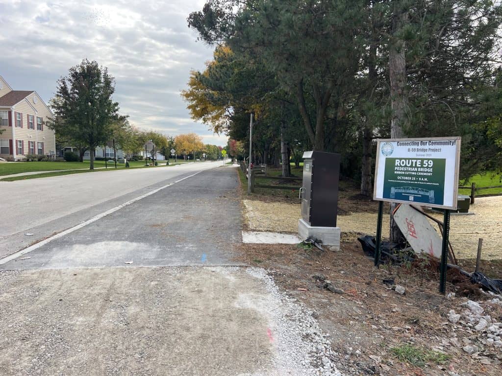 Road alongside suburban neighborhood with bicycle path and community signage.