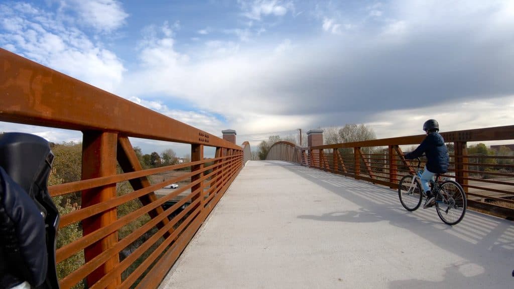 Scenic suburban Chicago bike trail on a clear day with a cyclist riding over a bridge.