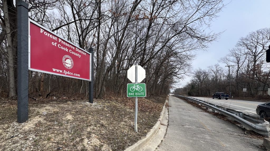 Bicyclist bike route sign along a trail off a suburban Chicago road with trees.