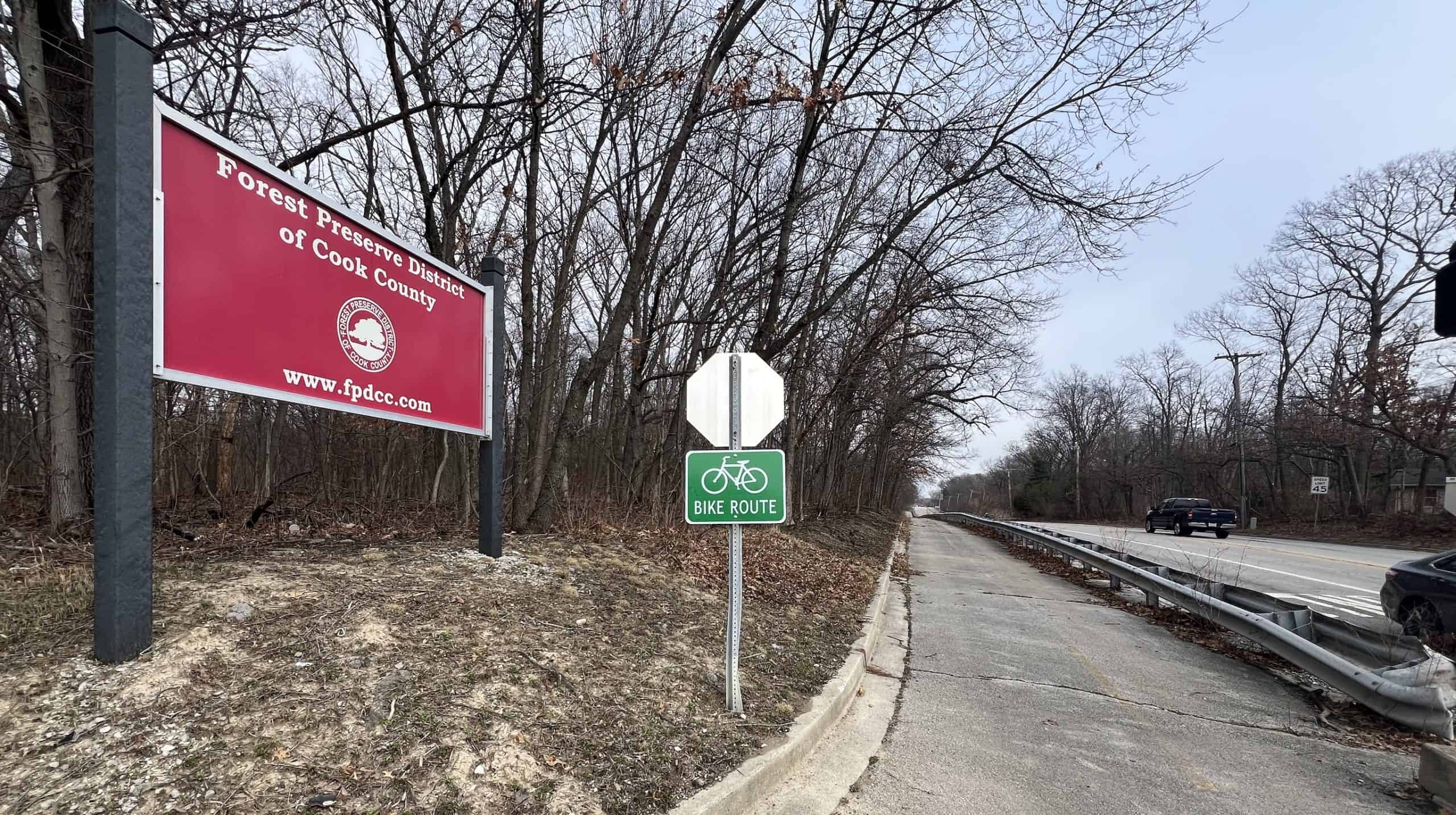 Bicyclist bike route sign along a trail off a suburban Chicago road with trees.