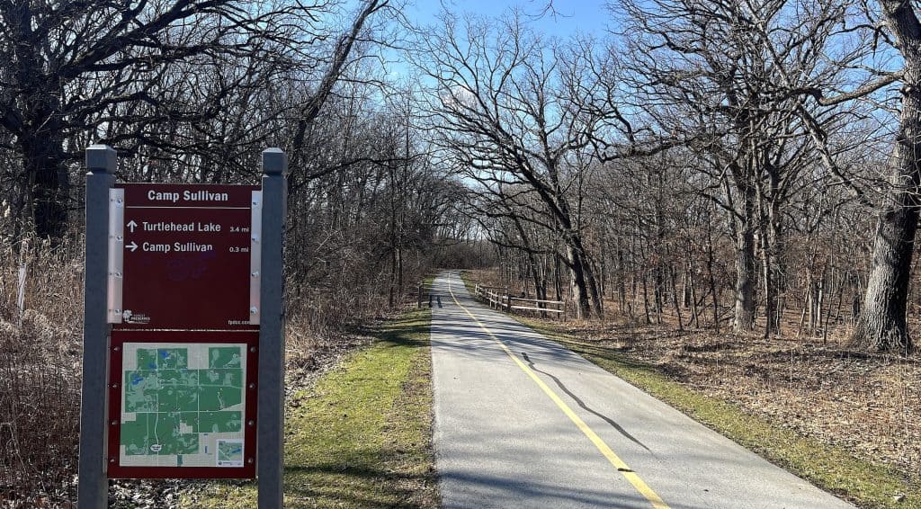 A scenic bike trail along Tinley Creek with trees and a trail map sign.