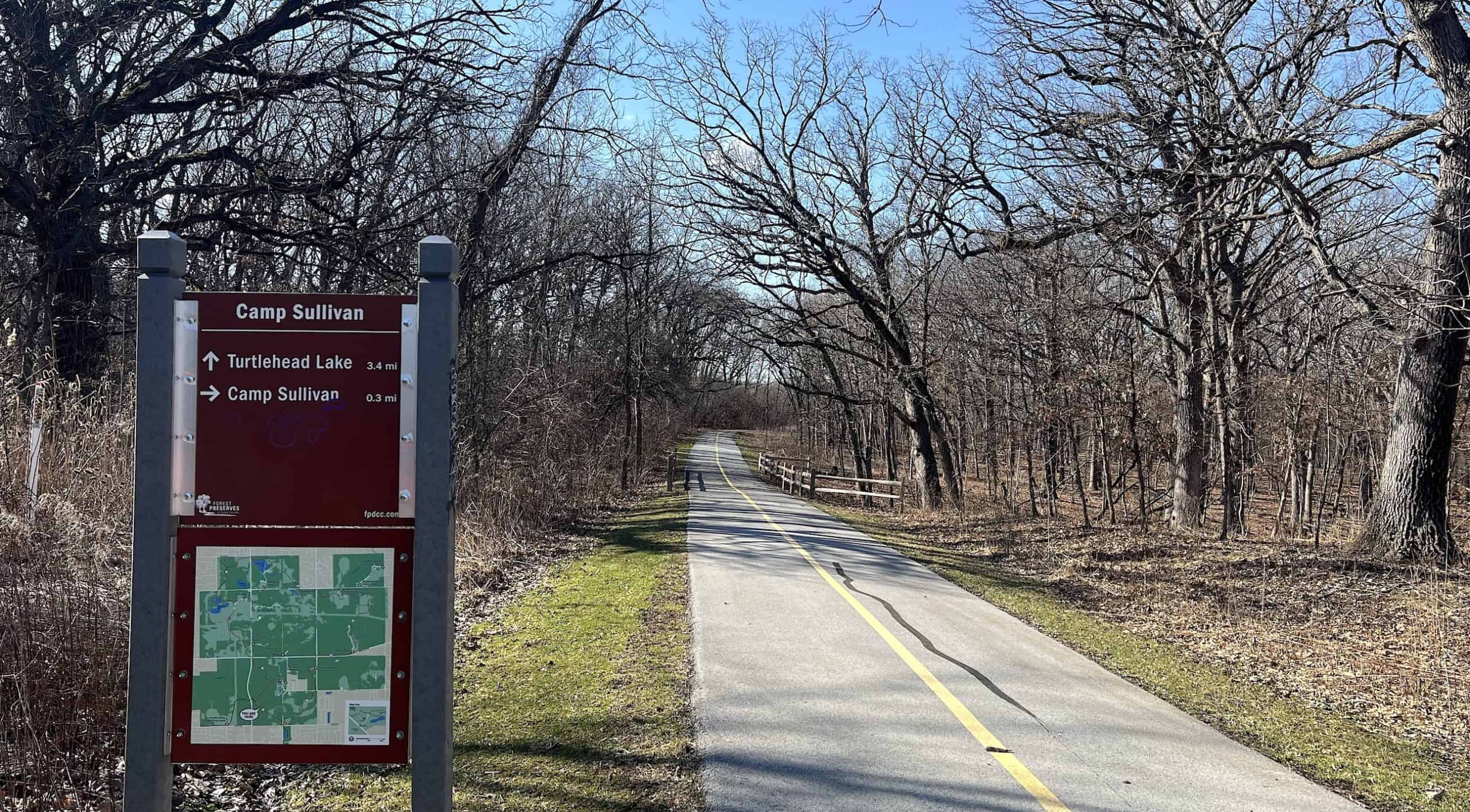 A scenic bike trail along Tinley Creek with trees and a trail map sign.
