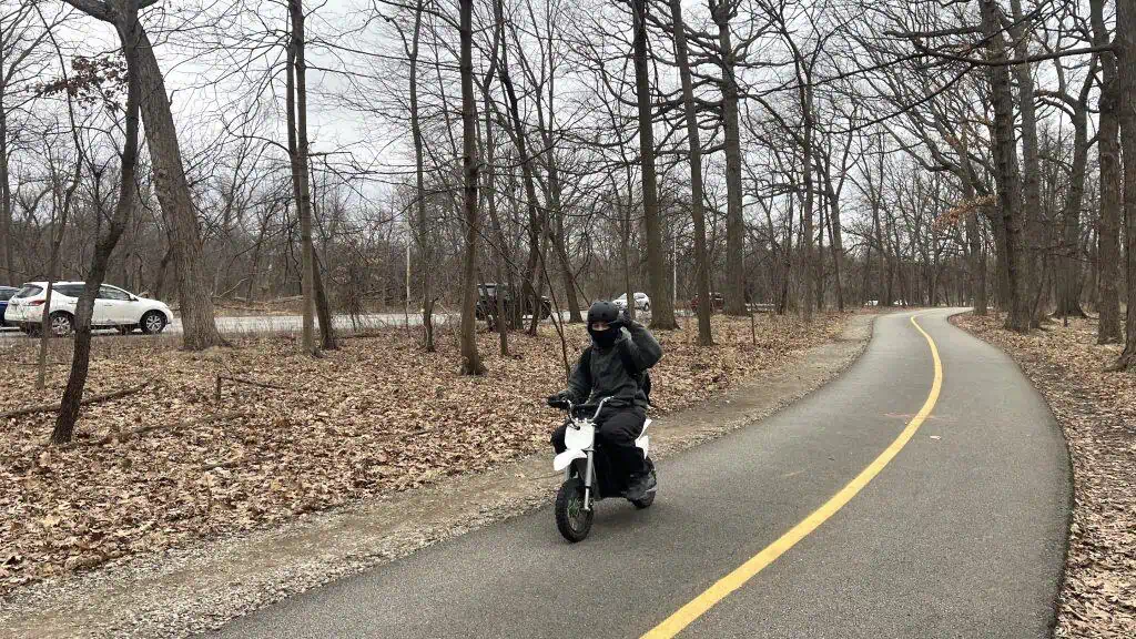 A cyclist riding an e-bike on a winding forest trail in suburban Chicago during daytime.