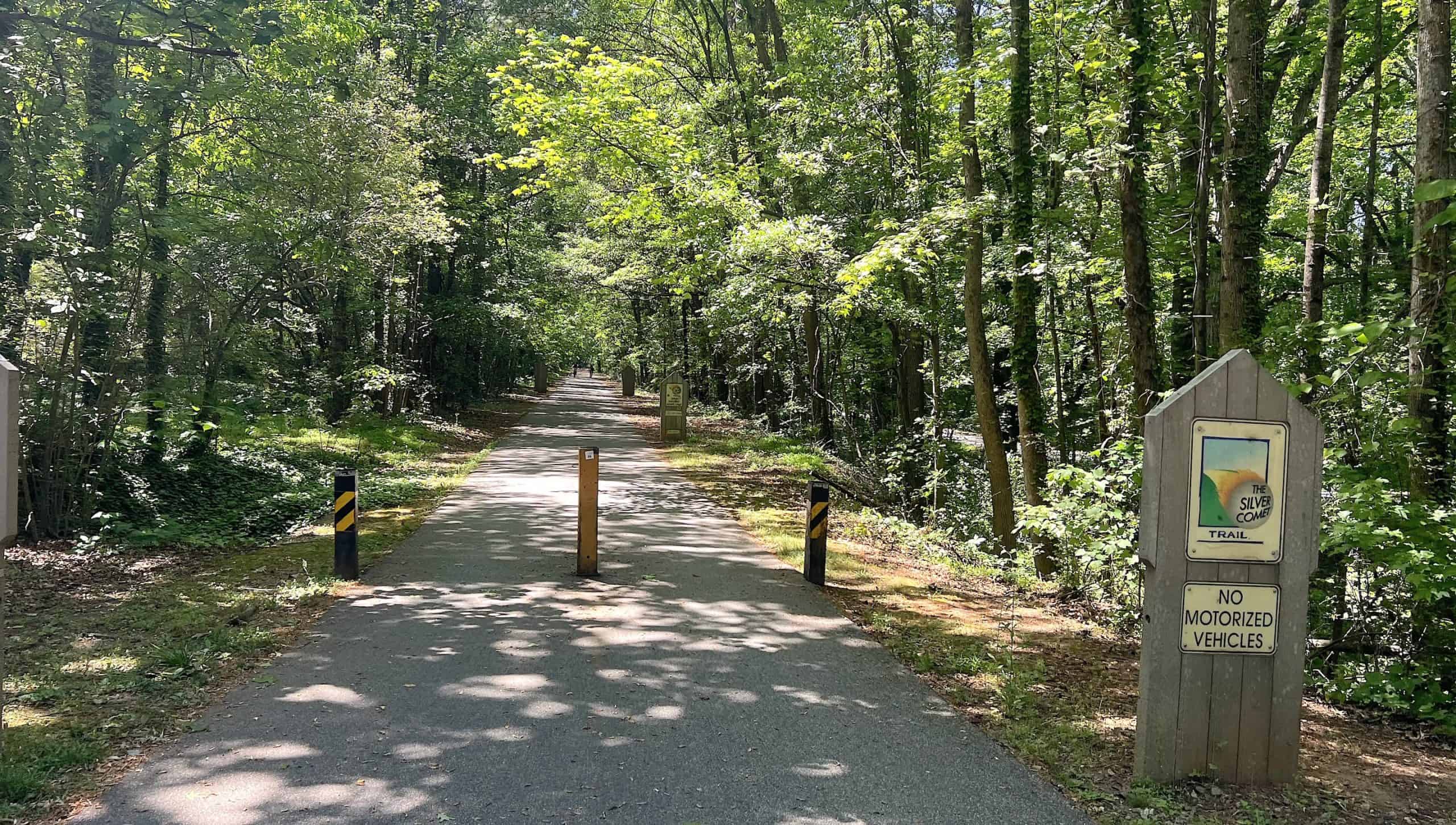 A lush green forest trail with a "No Motorized Vehicles" sign and a paved bike path.