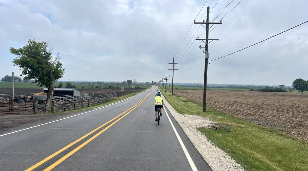 Cyclist riding on a rural road in Suburban Chicago with open fields and power lines.