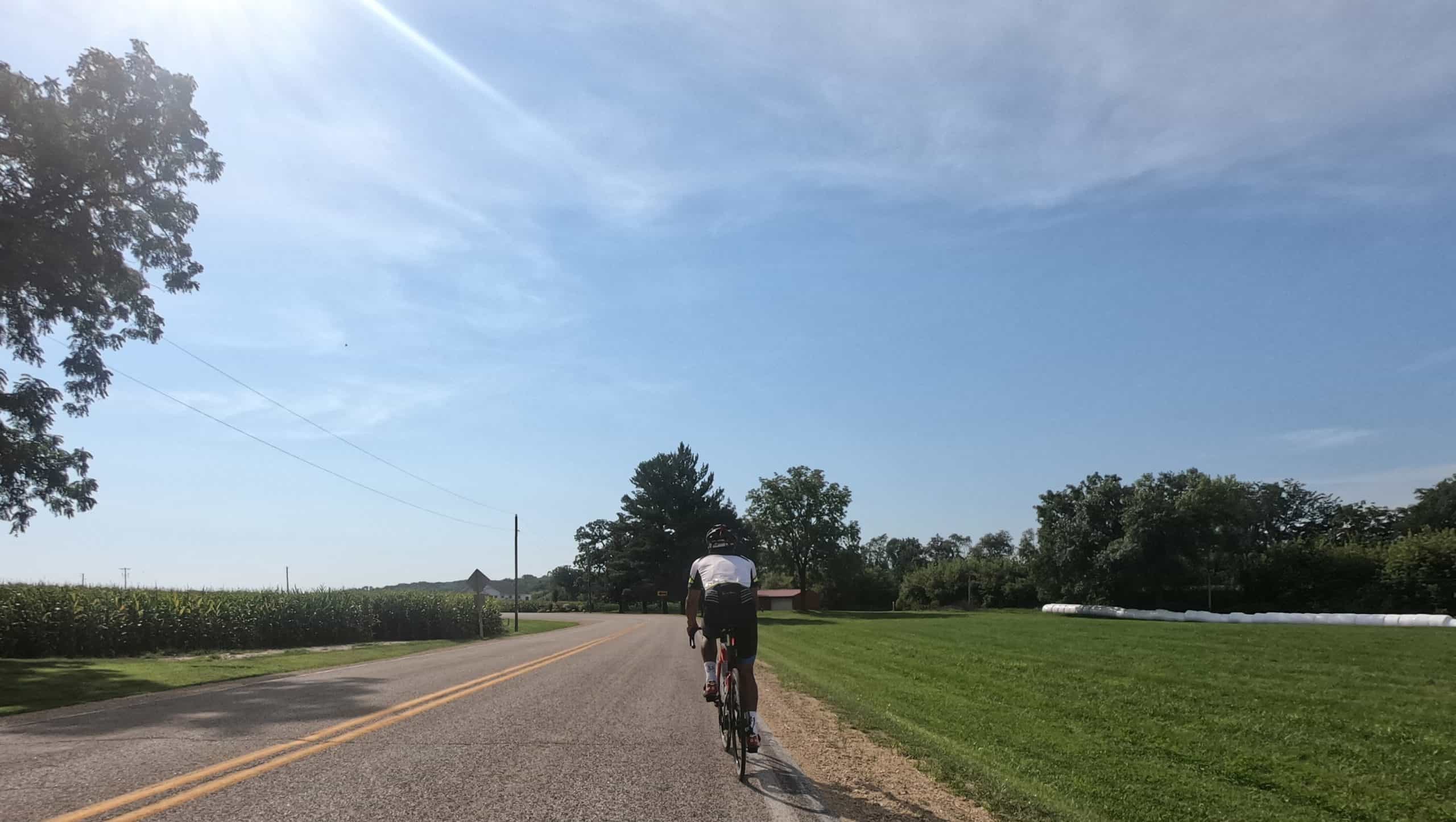 Cyclist riding on a rural road in suburban Chicago with clear blue sky.