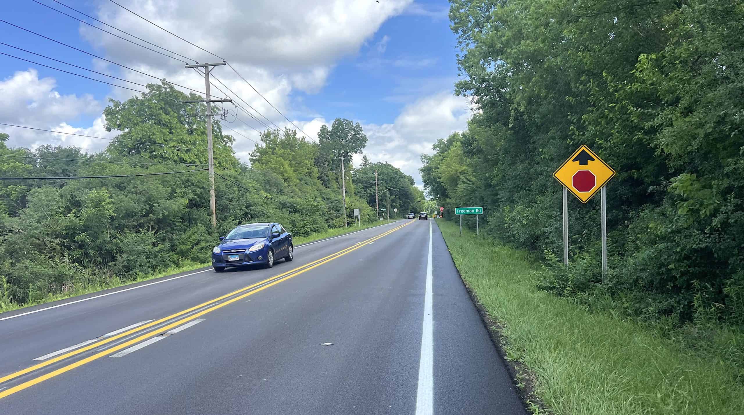 View of Ela Road with a bicycle warning sign and a passing car in suburban Chicago.