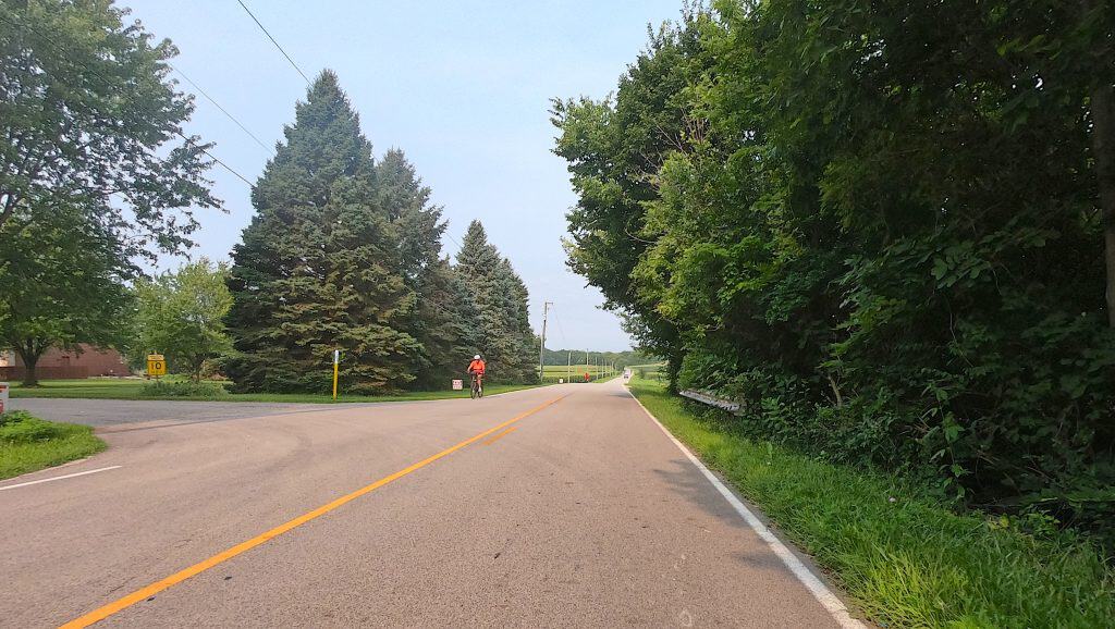 Scenic suburban road in Kendall County with trees and cyclist in distance.