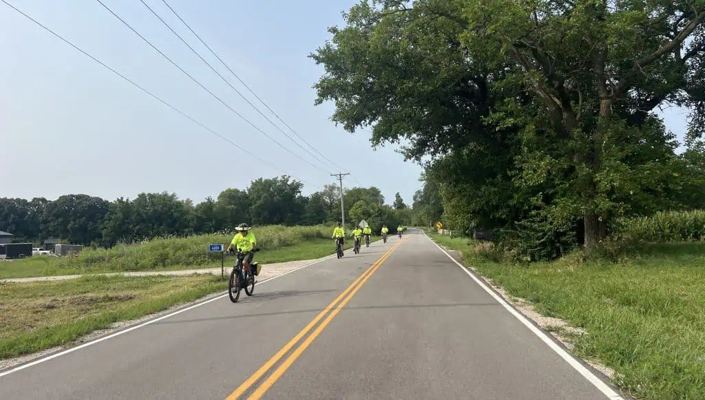 Cyclists riding on a rural road with trees and open fields in suburban Chicago.
