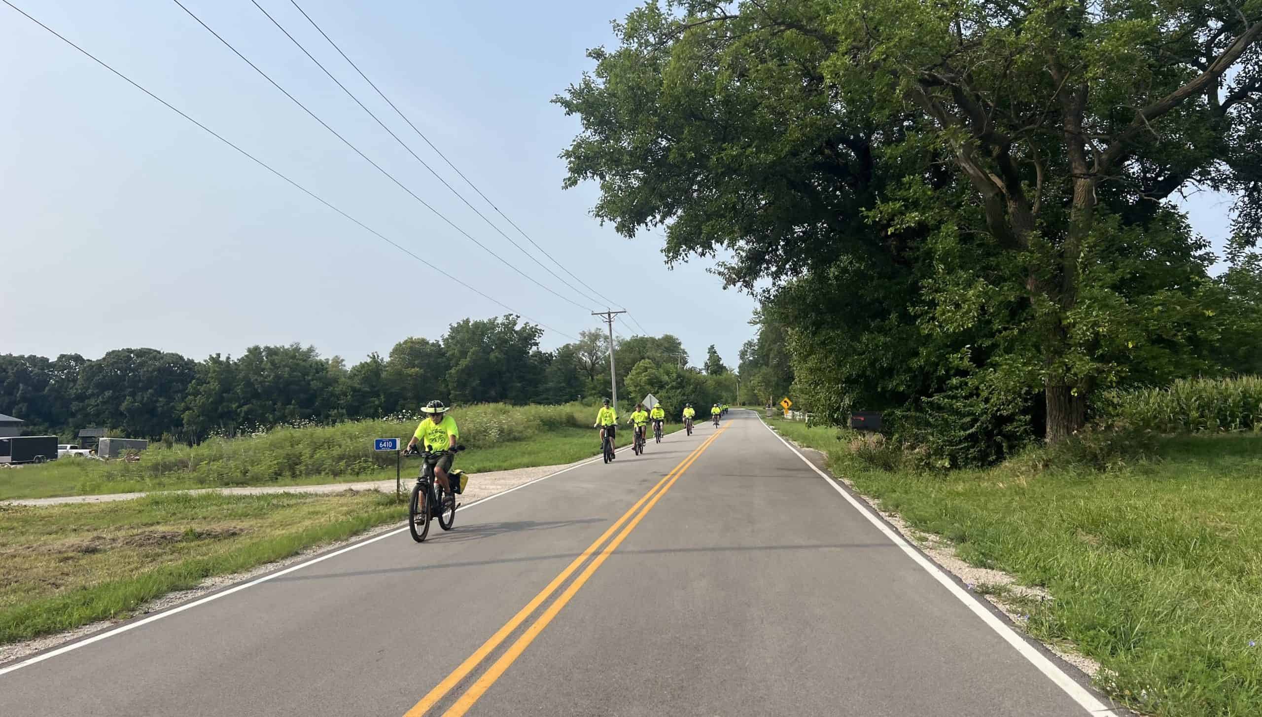 Cyclists riding on a rural road with trees and open fields in suburban Chicago.