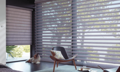 Contemporary living room featuring large windows with horizontal blinds, a cozy armchair, a cat sitting on the floor, and a scenic outdoor view.
