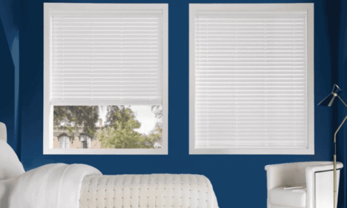 Bright bedroom featuring two large windows with white horizontal blinds, blue walls, and a white bed and chair, creating a clean and contemporary look.