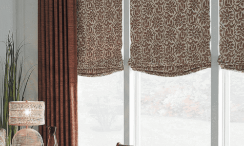 Living room window with patterned valances and matching curtains, complemented by decorative pillows and a side table with a lamp.