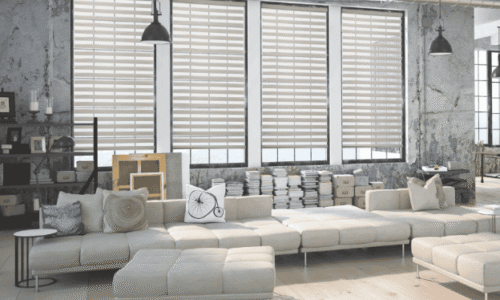 Spacious industrial-style living room with large windows, white sectional sofa, and minimalist decor in a loft setting.