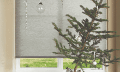 Small decorated Christmas tree on windowsill with hanging ornaments and holiday decorations around it.