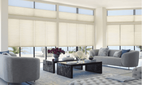 Bright modern living room with large windows, white blinds, and stylish furniture including a sofa, armchair, and coffee table.