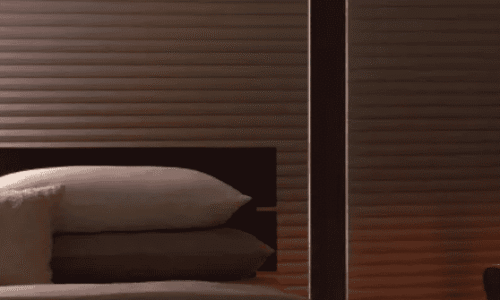 Cozy bedroom with wooden wall panels, neatly made bed with pillows, and warm lighting creating a relaxing atmosphere.