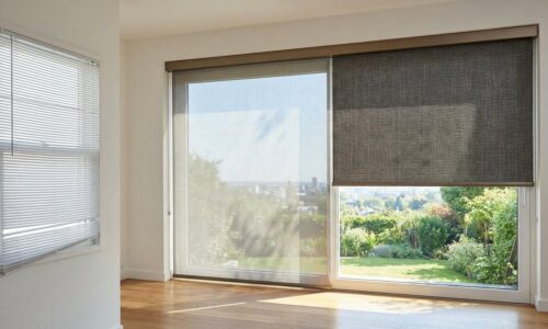 Bright living room with large glass sliding doors and window blinds, overlooking a lush green garden outside.