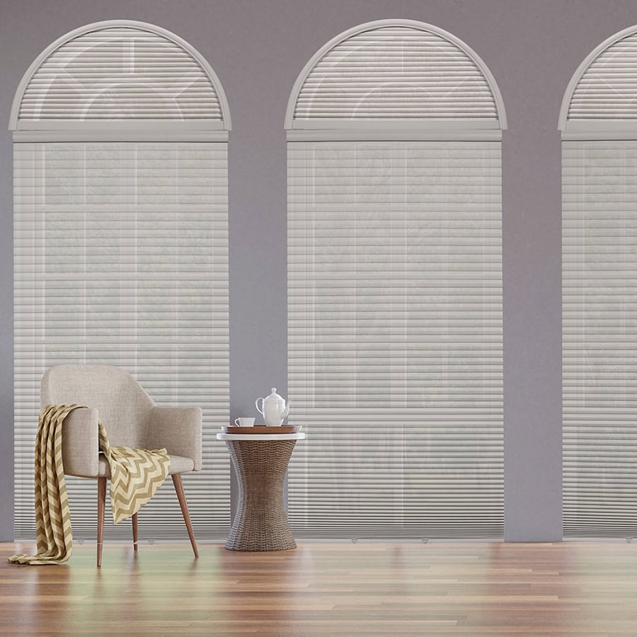 Bright interior with large arched windows and white blinds, featuring a comfortable beige armchair draped with a yellow blanket, and a small round side table with a teapot and cup, creating a relaxing.