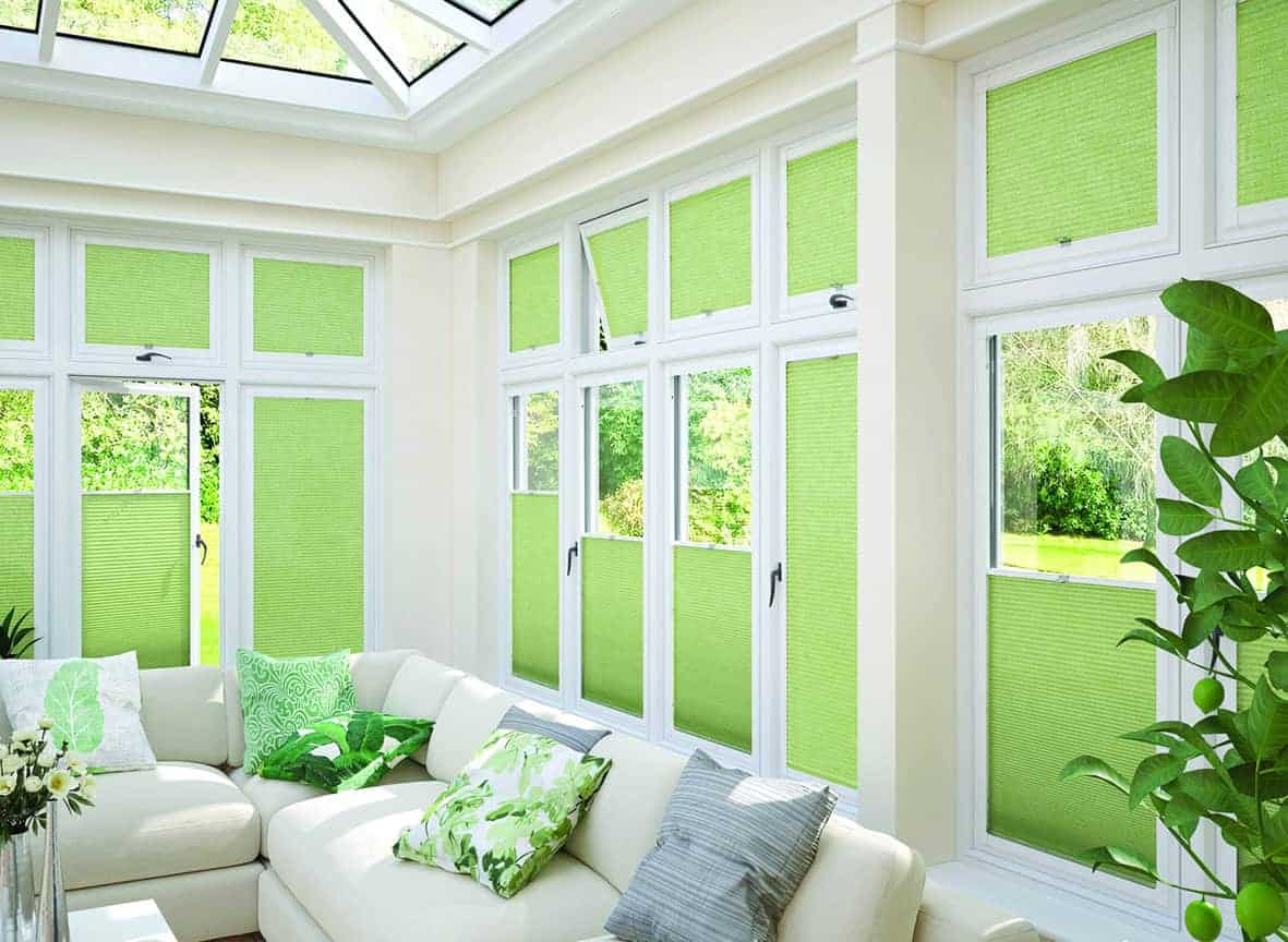 Bright sunroom featuring large windows with vibrant green blinds, white sofa with green and gray cushions, and lush outdoor scenery visible through the windows.