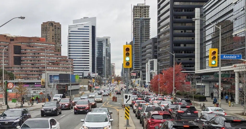 Busy city street in Toronto with cars, traffic lights, and high-rise buildings on a cloudy day.