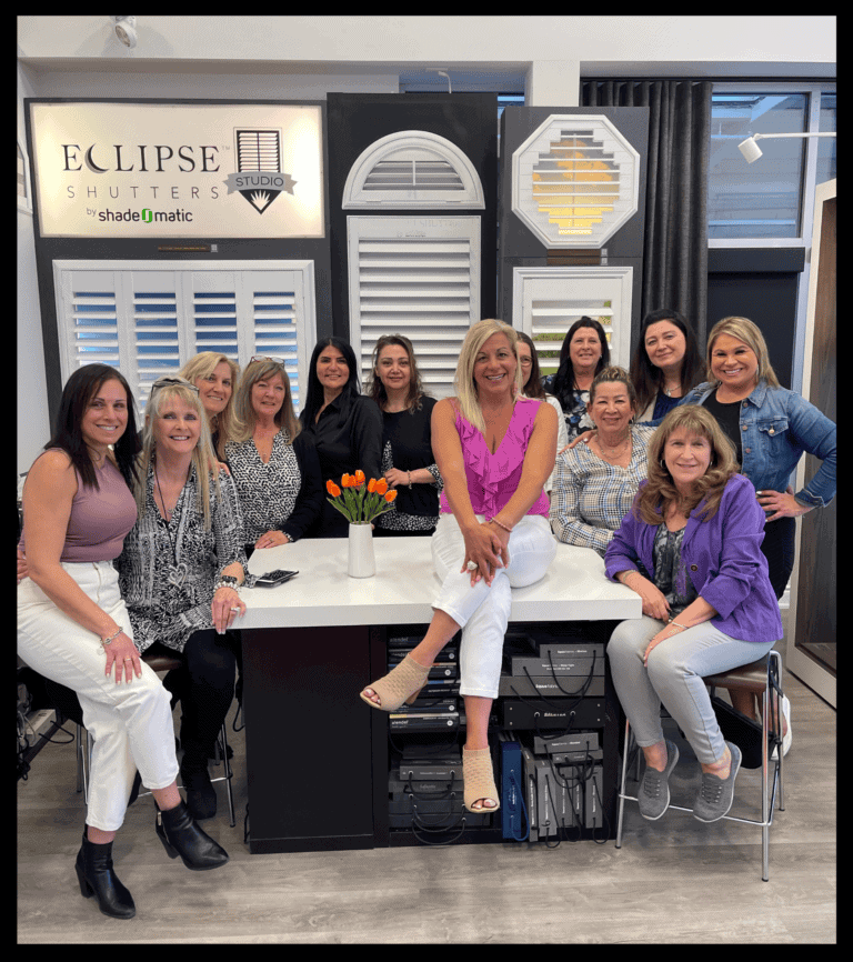 Group of women gathered in a showroom with window shutters and blinds, smiling and posing for a photo.