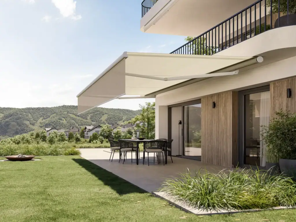 Contemporary house with a spacious outdoor patio, black dining table, and chairs, overlooking green hills and a clear sky.
