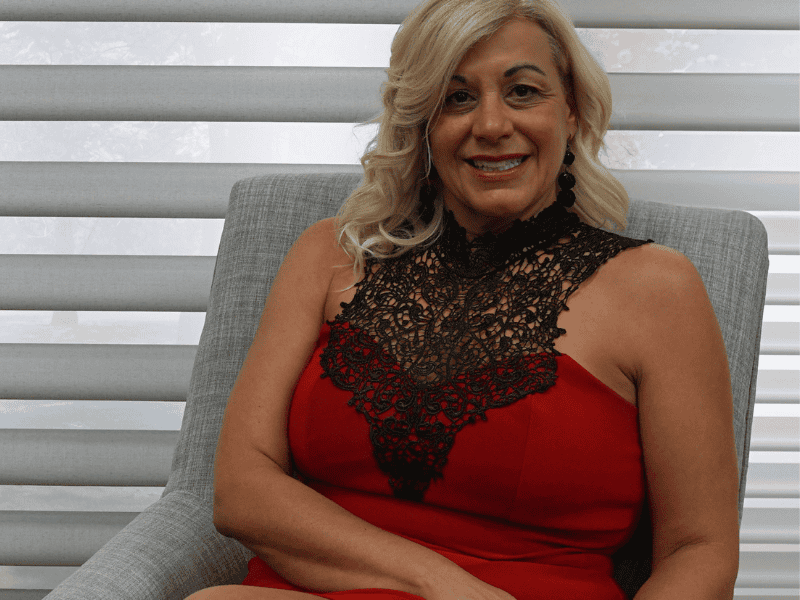 Elegant woman wearing a red dress with black lace detailing in a modern home setting.