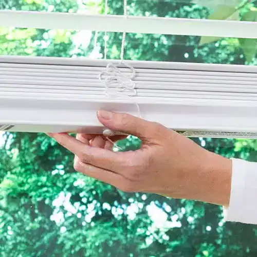 Smooth white window blinds with a hand adjusting them, showcasing high-quality window treatment options.
